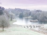 Painshill Park landscape garden overlooking the reinstated five arch bridge, frozen lake and grotto with the Gothic Temple in the background