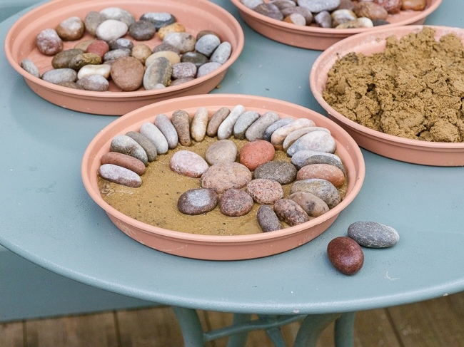 Making a pebble mosaic pattern. 2. Place pebbles iinto tray and bed in on top of wet sand