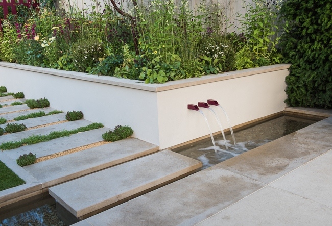 Pathway with stepping stone over a rill and water feature with raised beds behind