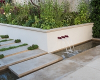 Pathway with stepping stone over a rill and water feature with raised beds behind