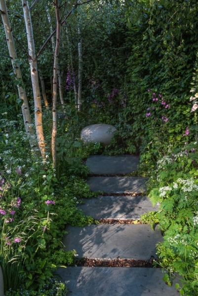 Pathway in a woodland garden leading towards a large stone shaped rock as a focal point