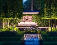 A pathway lead up to a contemporary cantalevered seating area with lighting in the early evening