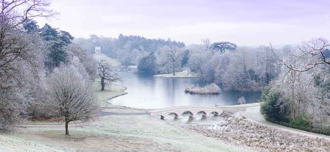 Painshill Park landscape garden overlooking the reinstated five arch bridge, frozen lake and grotto with the Gothic Temple in the background