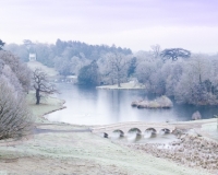 Painshill Park landscape garden overlooking the reinstated five arch bridge, frozen lake and grotto with the Gothic Temple in the background