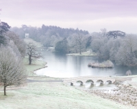 Painshill Park landscape garden overlooking the reinstated five arch bridge, frozen lake and grotto with the Gothic Temple in the background