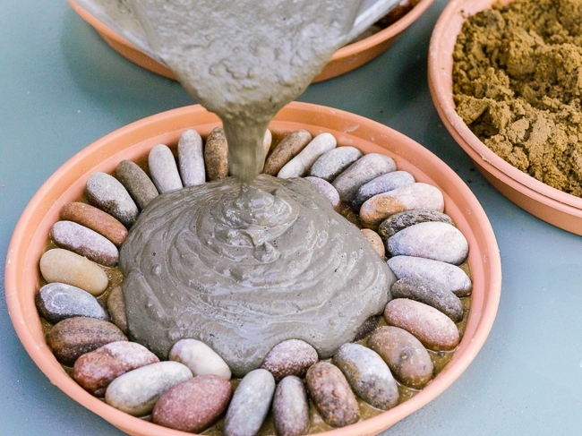 Making a pebble mosaic pattern. 3. Pour a mixture of quick setting cement over yhe top of your mosaic design.